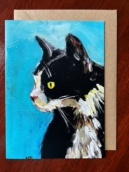 Greetings card depicting a black and white cat called Arthur painted against a blue background. Brown envelope visible behind card.