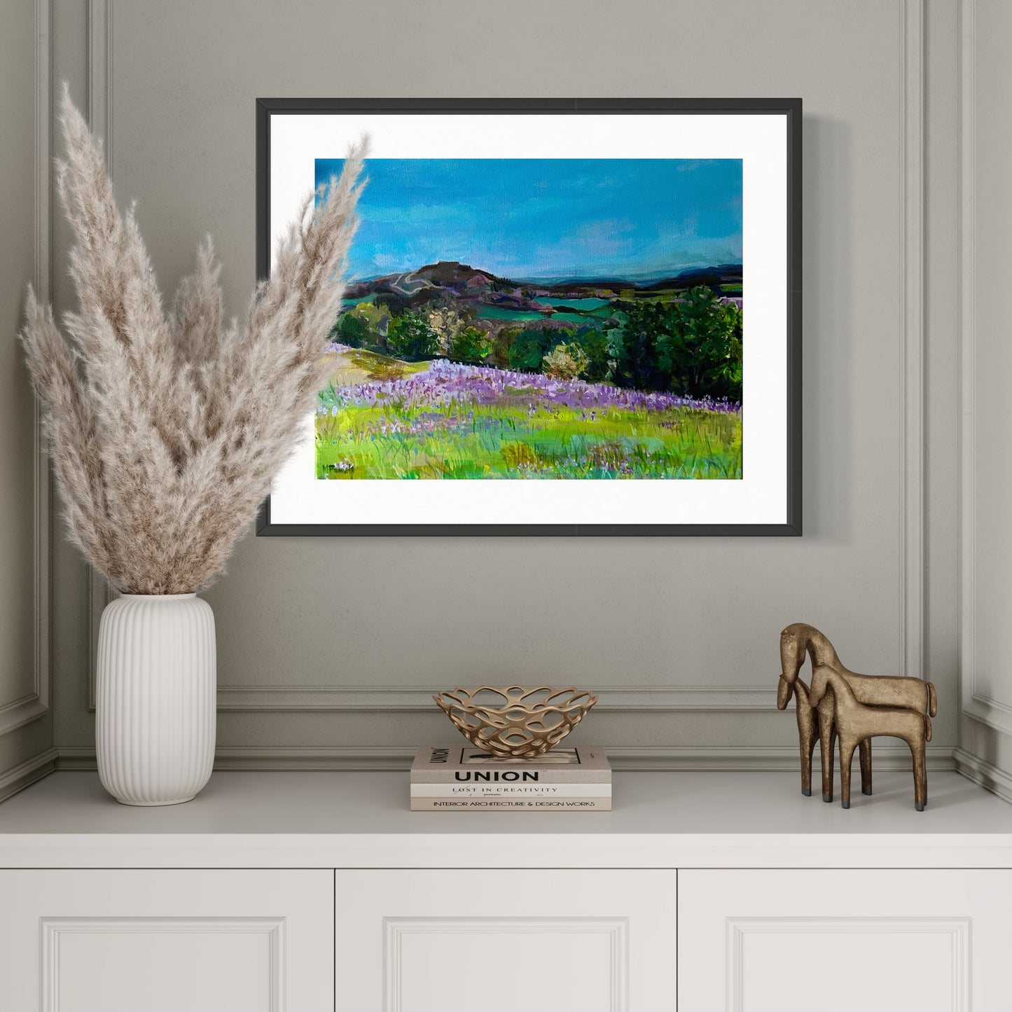 Framed print of Bluebells in the Malvern Hills from original painting by Margaret Powell. Displayed in a white alcove with white dried grass in a vase in front.