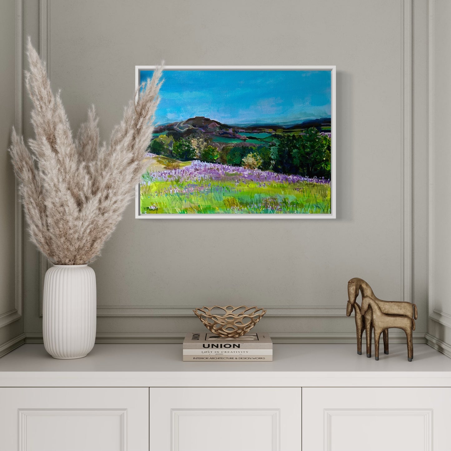 Framed Original painting of bluebells on the Malvern Hills by Worcestershire artist Margaret Powell. Displayed against a white wall with white dried grass in a vase in front.