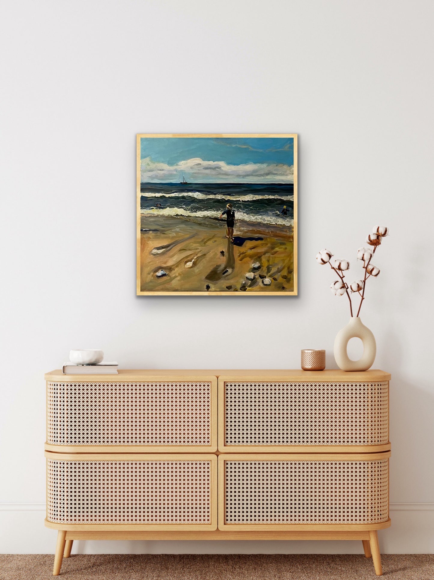 Original painting of Girl on Caswell Bay Beach by Margaret Powell. Displayed in a light brown wood frame on white wall with furniture in front.