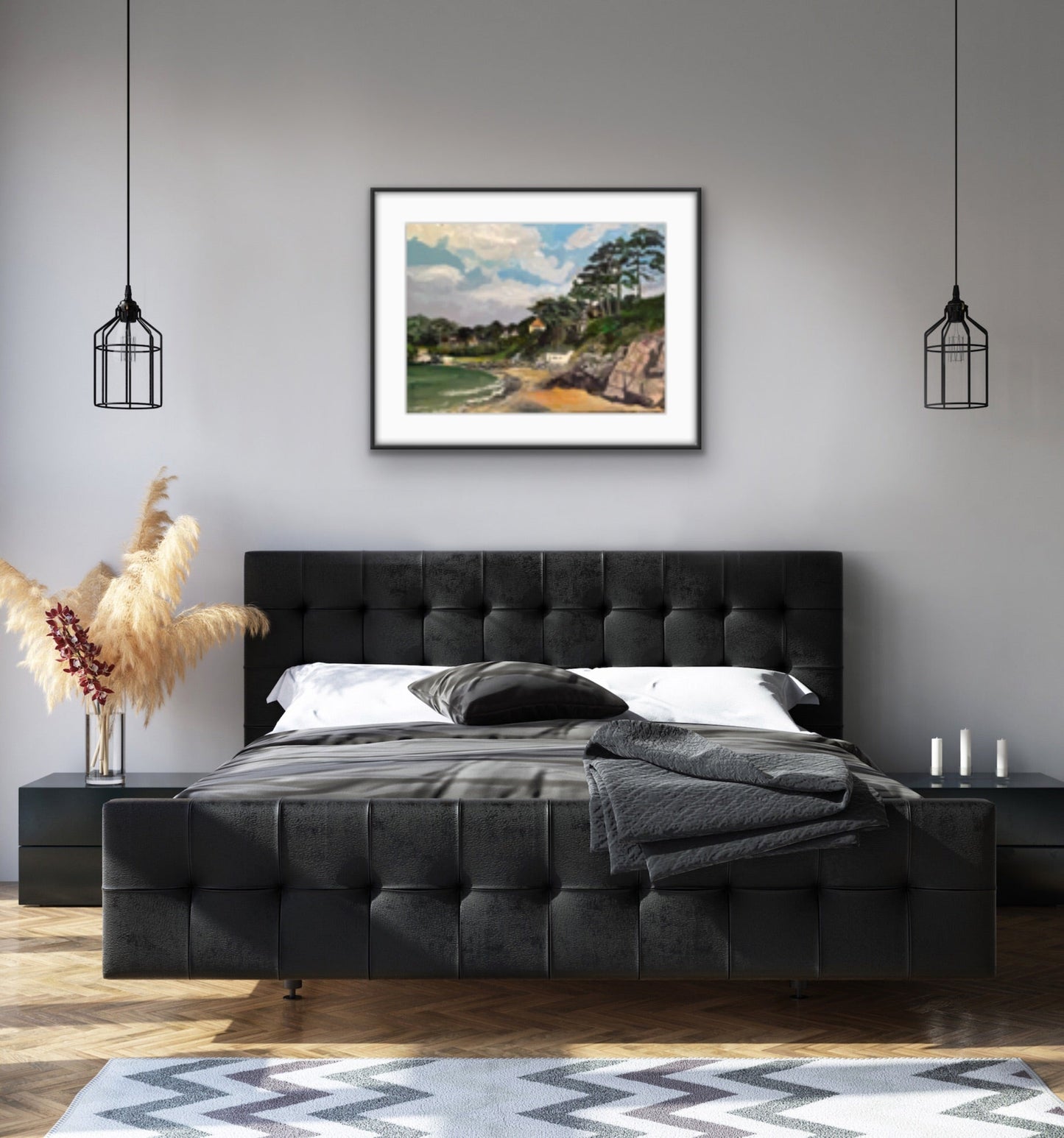 Painting of Caswell Bay in the Gower, Wales with white clouds in a blue sky and rocks and sea in foreground with trees and houses on the headland. Displayed on a grey wall with a dark grey bed in the foreground.