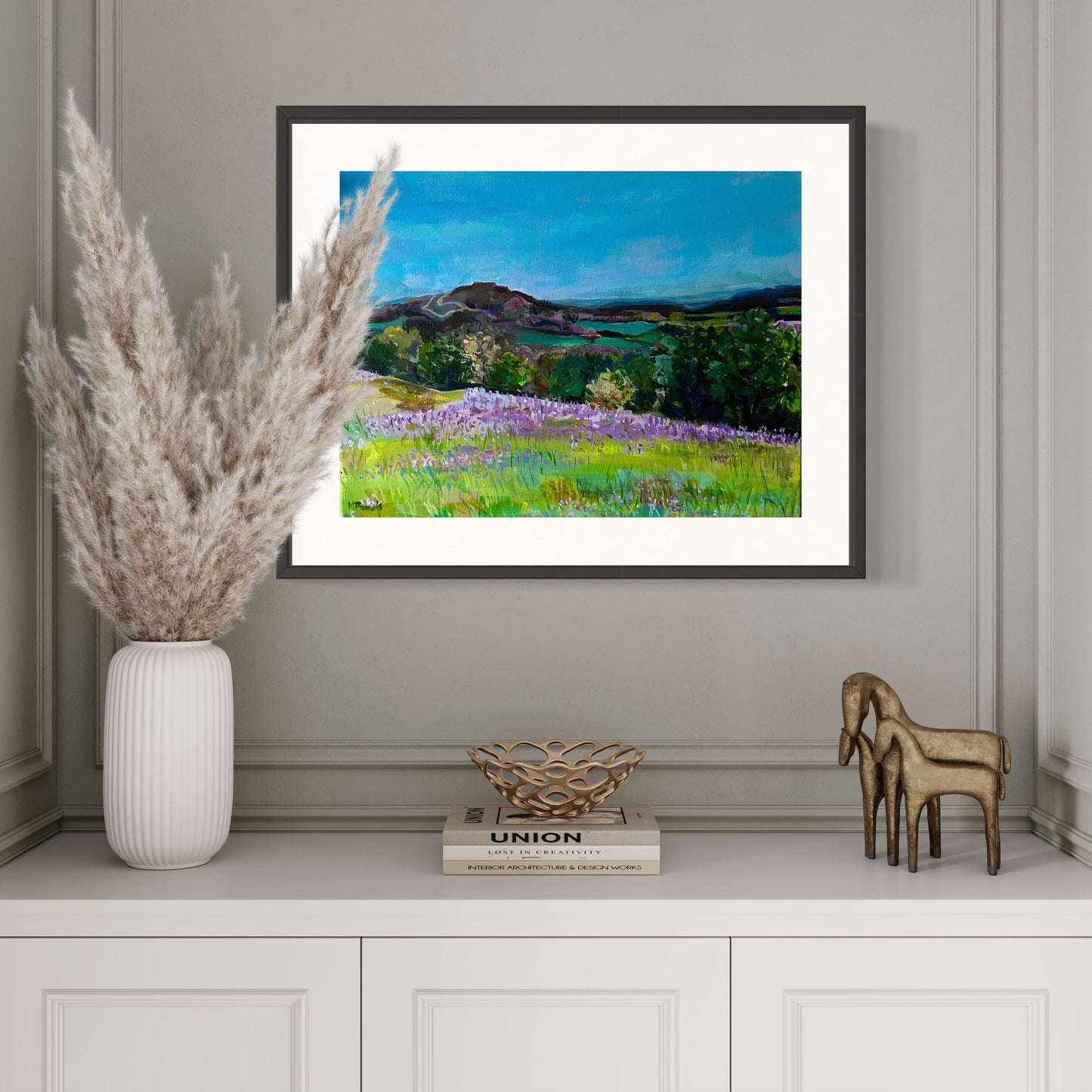 Framed print of Bluebells in the Malvern Hills from original painting by Margaret Powell. Displayed in a white alcove with white dried grass in a vase in front. 