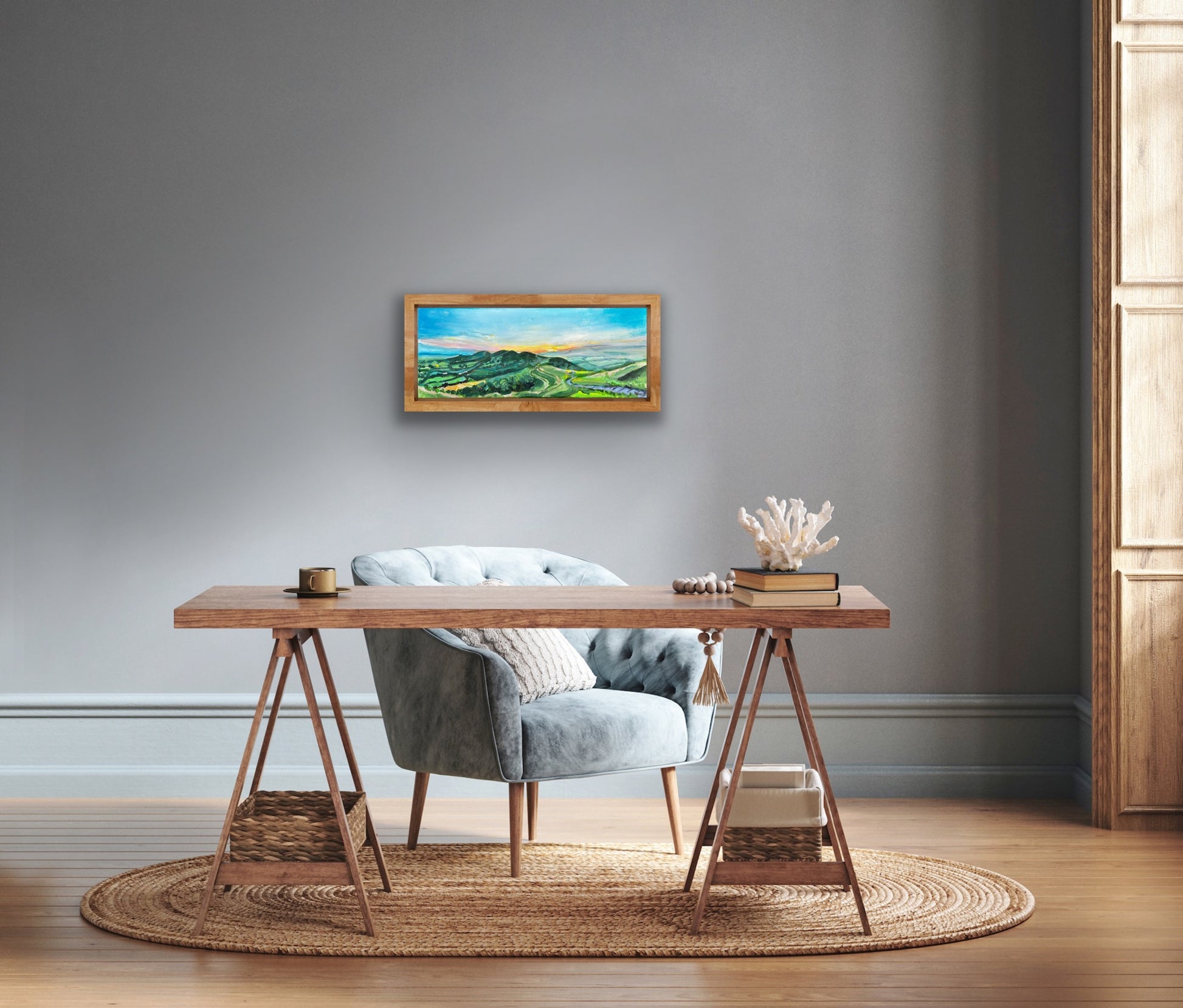 Original painting of Dawn at the Malvern Hills by Worcestershire Artist Margaret Powell displayed on a grey wall with furniture in foreground