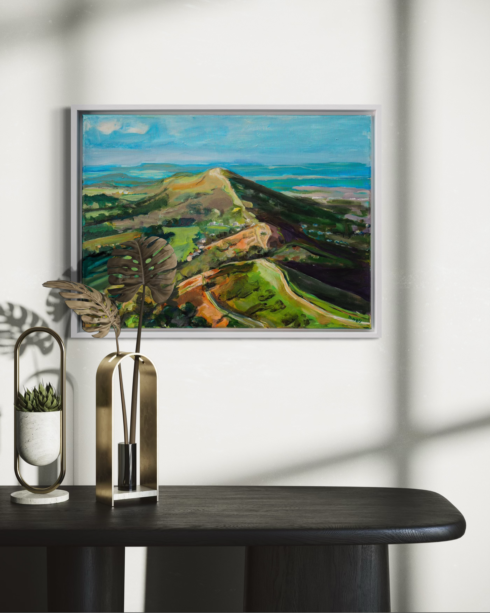 Framed Malvern hills original acrylic landscape painting on a wall above a dark surface with decorative items.
