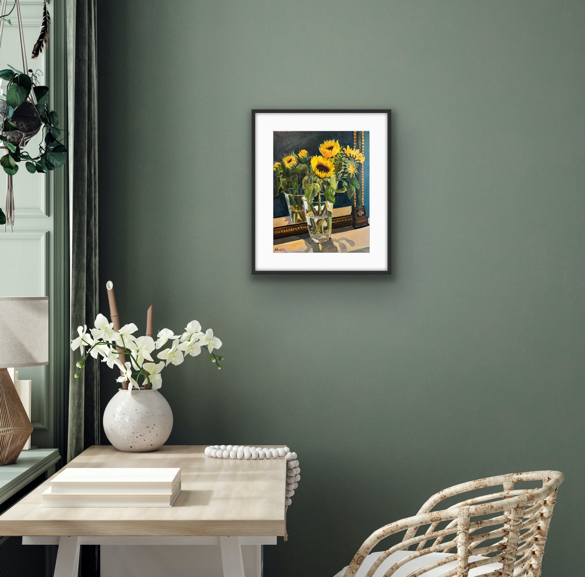 Print of a fine art painting of sunflowers displayed in a vase in front of a vintage mirror. Print framed in a white frame and displayed on a grey wall behind a white table and chair. 