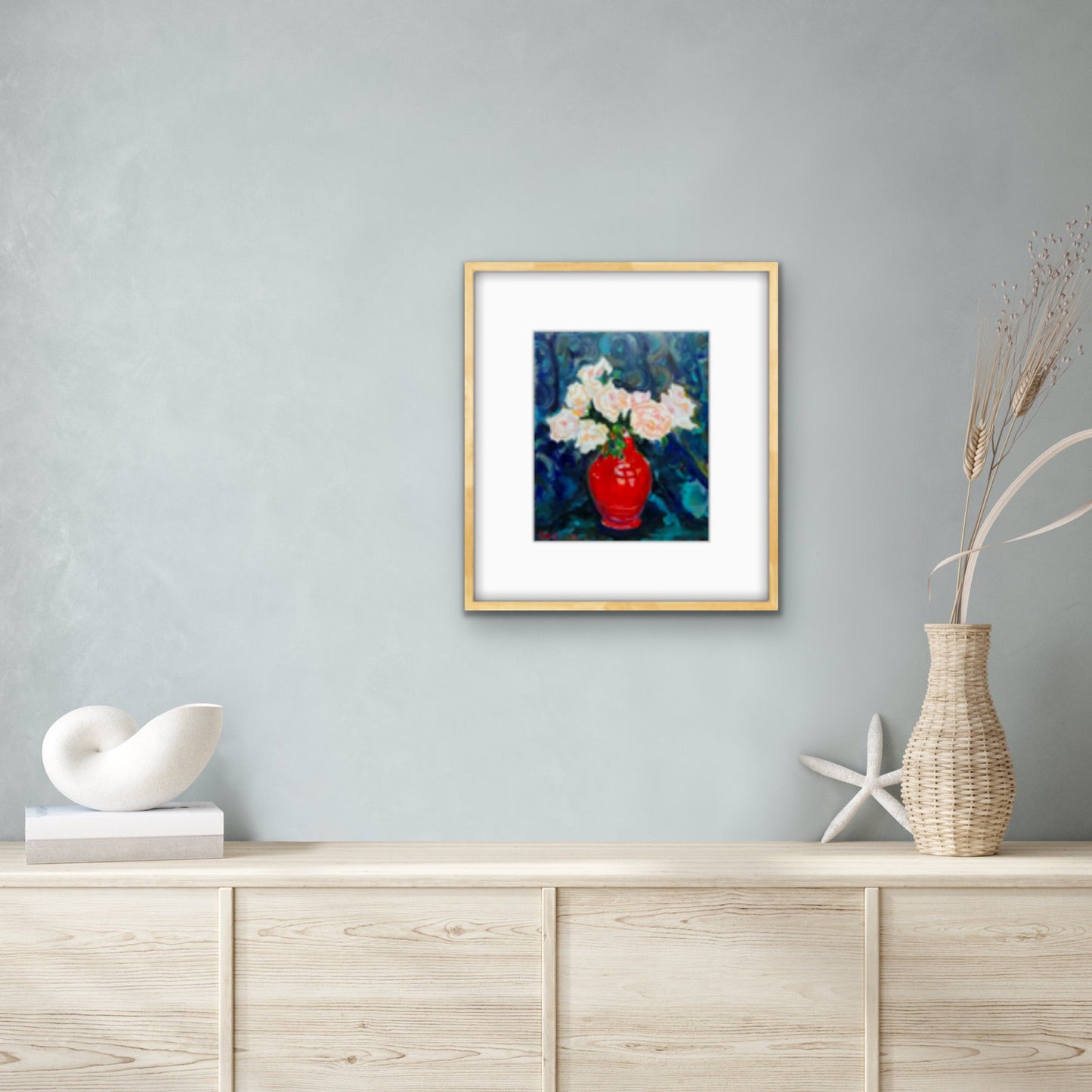Framed print of Fine art painting of Blush Roses in a Red Vintage Vase.  Displayed against a light grey wall with light wooden furniture in front. 